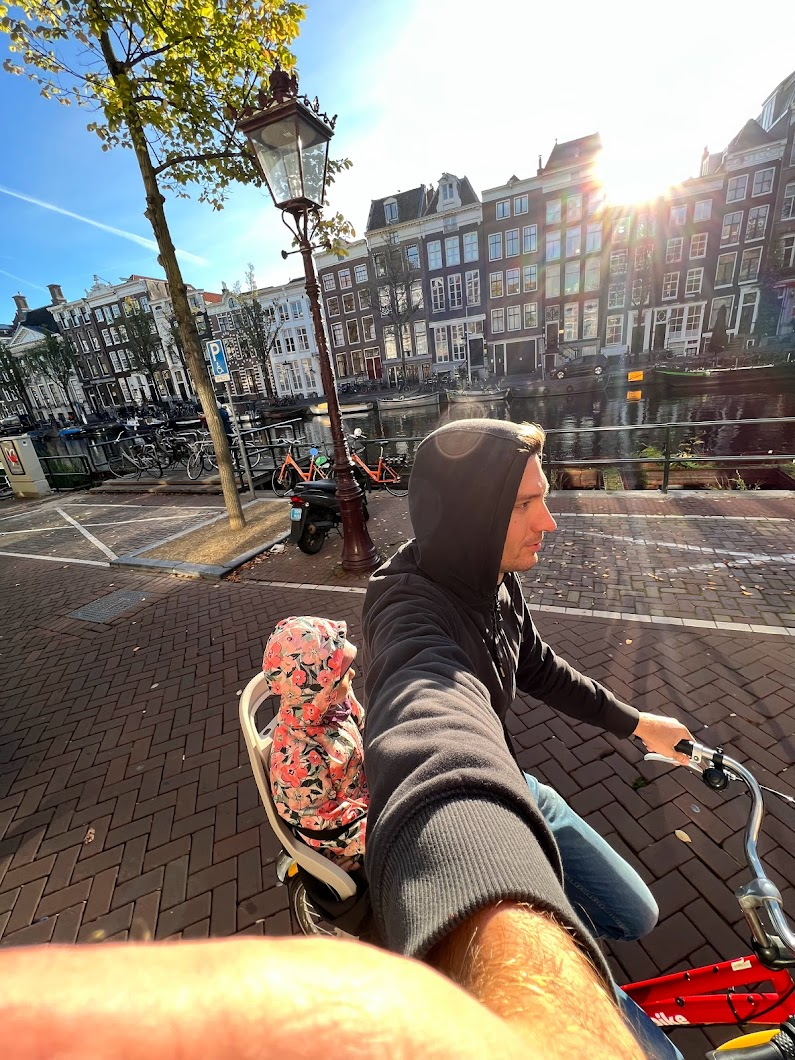 Tom riding a bike with his daughter in a child seat on the back, exploring the streets of Amsterdam, highlighting the family-friendly nature of biking in the Netherlands.